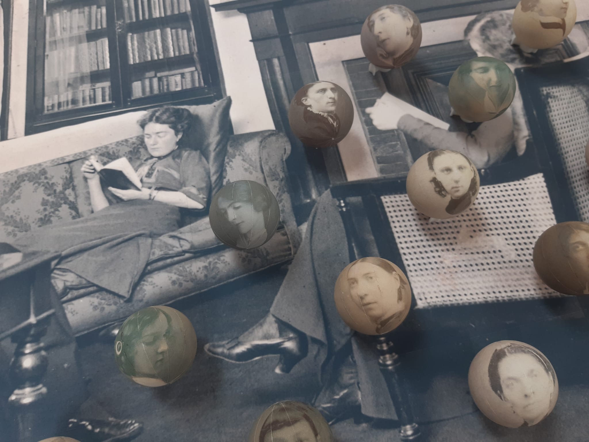 Numerous spheres rest on top of a black-and-white photograph of two women sitting and reading. The spheres each depict black-and-white images of women's faces.