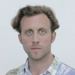 A headshot of Pádraic E. Moore. He has short, blonde hair and wears a multicoloured shirt.