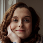 Laura O'Shea poses for a photograph with her face cupped in one hand. She has long, brown hair.