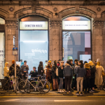 A crowd of people talk to one another outside Ormston House in the evening.
