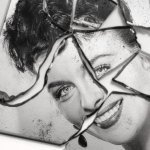 A black-and-white image of a smiling woman on a pane of glass broken into pieces. She has short, dark hair.