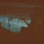 Jon Collin plays the guitar in a dark room. To the right of the image, there is a vertical red stripe with an uneven edge.