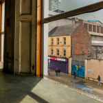 A window with wooden slats faces out onto a street. The camera is positioned indoors and looks through the window.