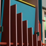 A complex, colourful arrangement of painted plywood, wooden dowels and bright orange rope. In the background, a windowpane glistens in metallic hues, with a barely-legible sign overhead reading 'KUNSTVER...'.