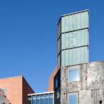 The Mac building. The lower, grey segment has a slanted roof, and the higher section has glass walls with slanted divides between them.