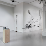An installation view of 'Bíodh Orm Anocht' at Ormston House. To the left in the foreground, an egg in a travel case is presented on a wooden plinth. Two sculptures and a large drawing are presented on off-white walls. In the background to the right, a ceramic and graphite artwork is presented at the base of a pillar.